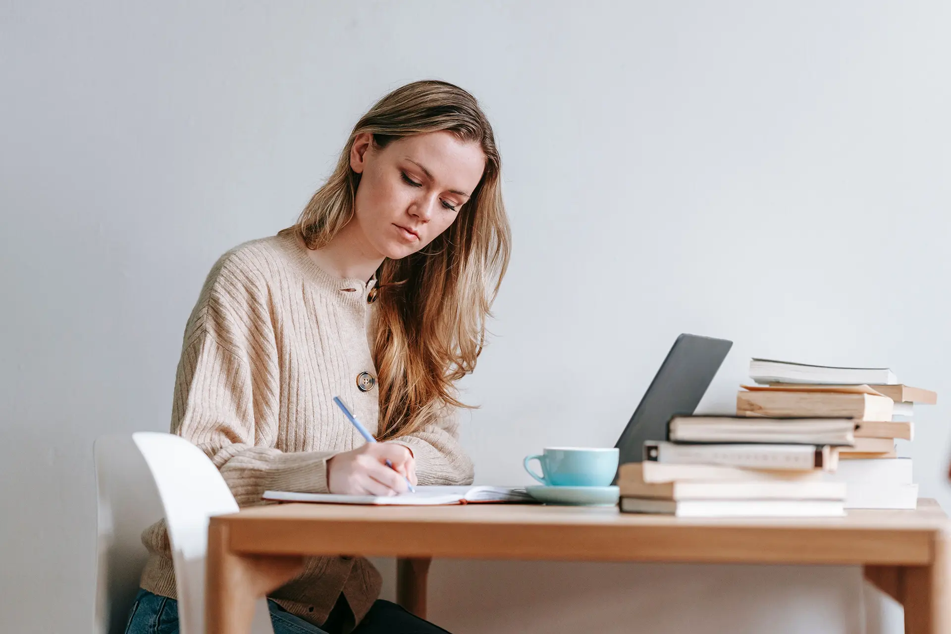 Young woman sitting at a desk writing with coffee and a laptop